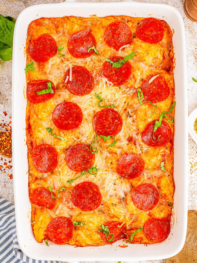 A baked pepperoni pizza casserole in a rectangular dish, topped with melted cheese and fresh basil.