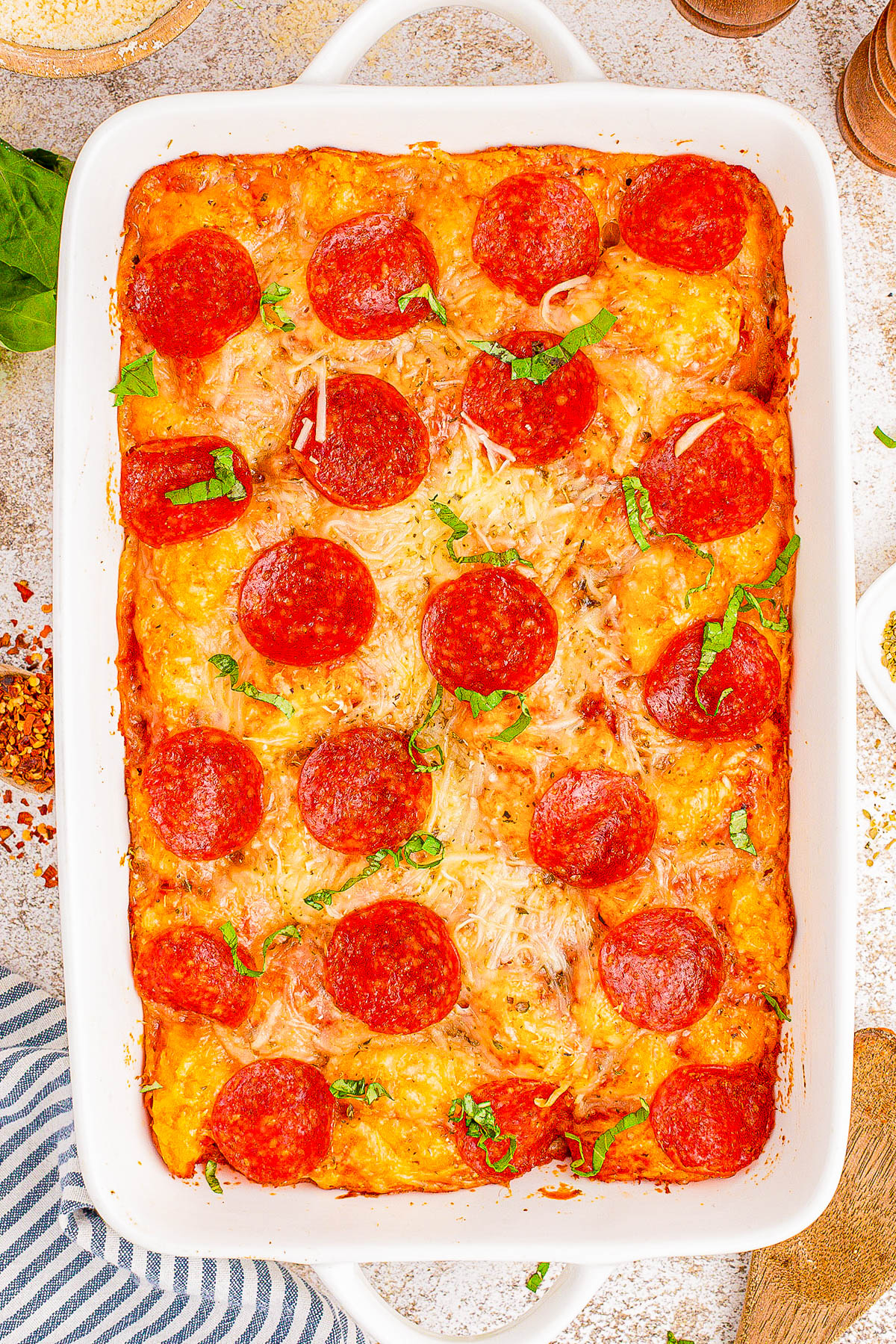 A baked pepperoni pizza casserole in a rectangular dish, topped with melted cheese and fresh basil.