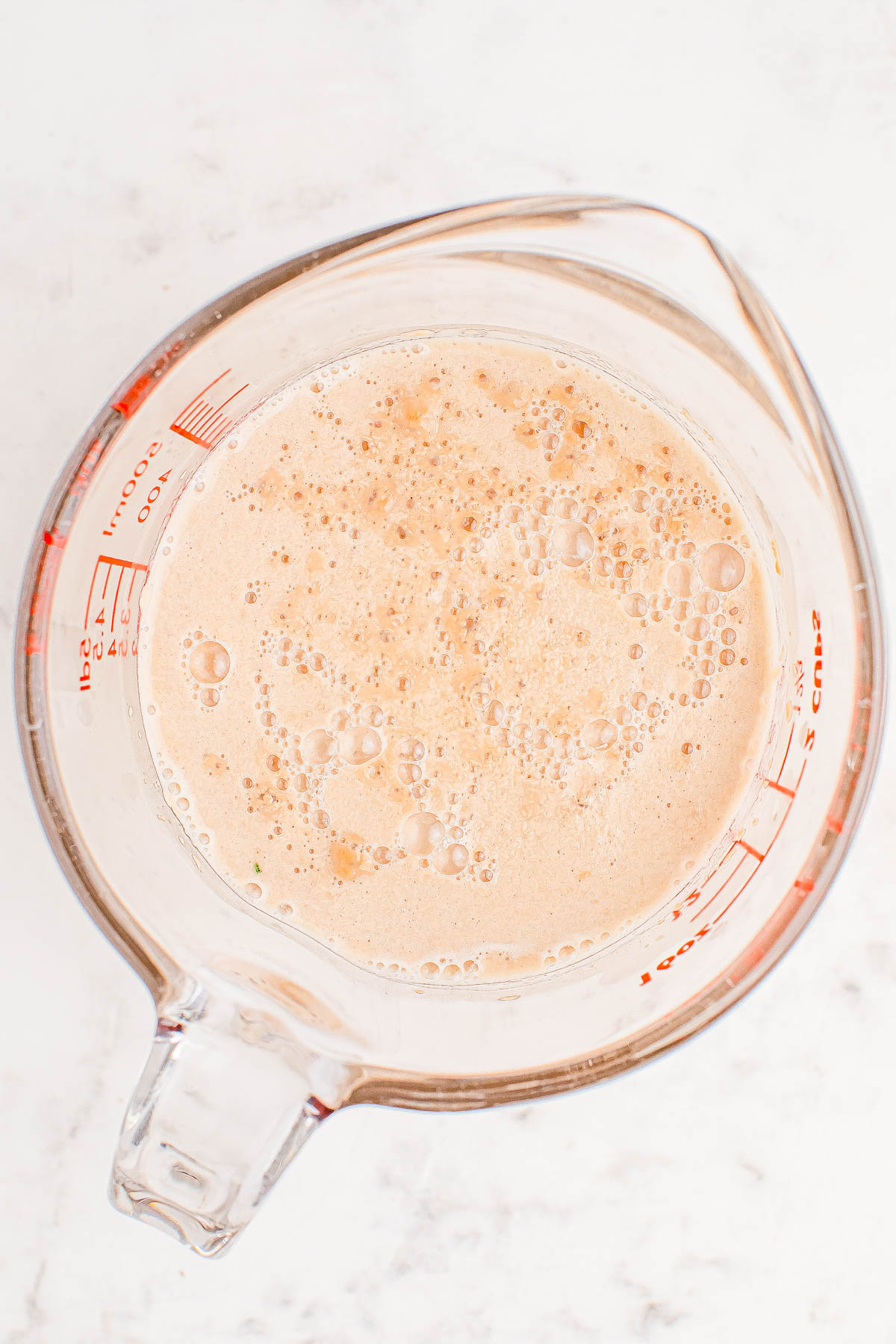 A clear measuring cup filled with a frothy brown liquid, placed on a white surface.