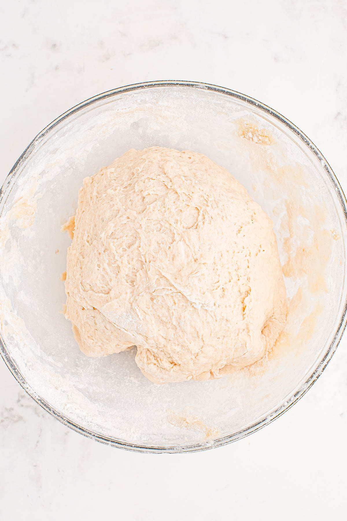 A ball of bread dough in a glass bowl on a marble surface.