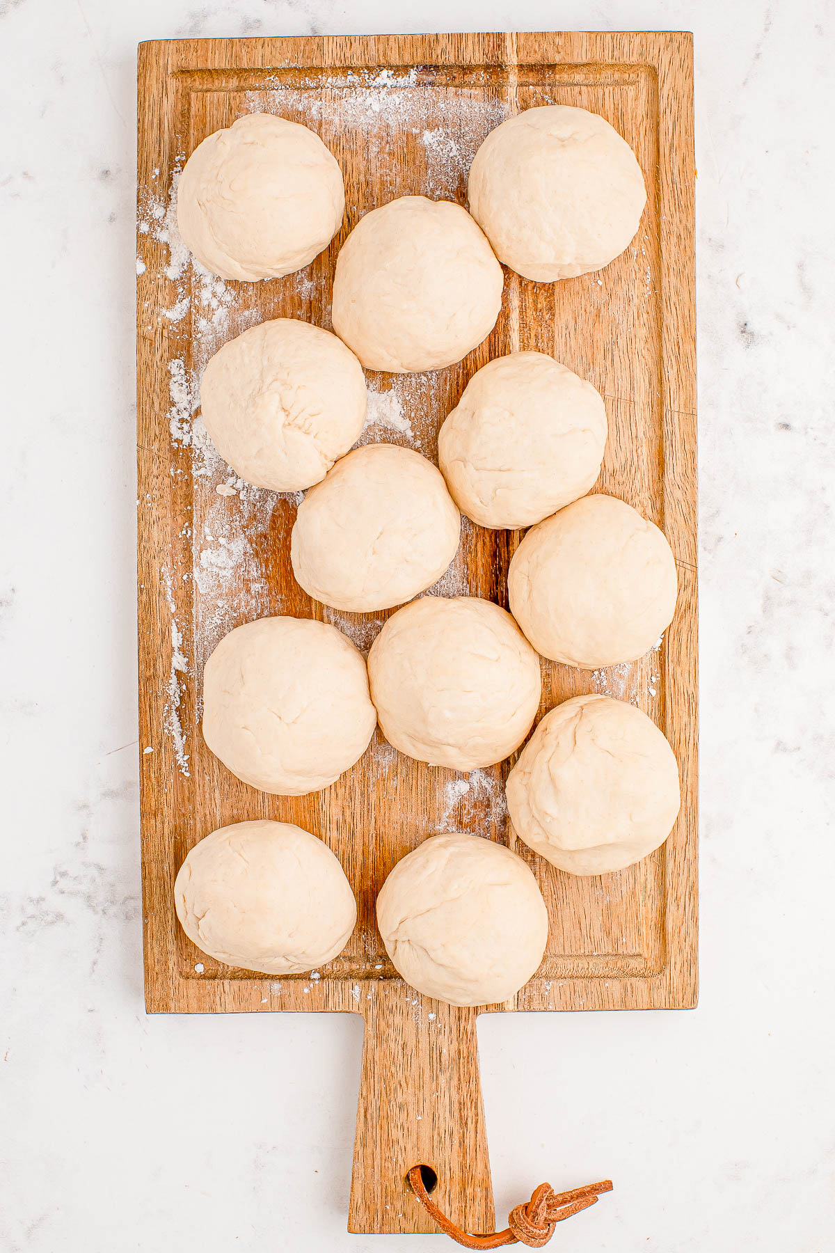 Twelve round dough balls on a wooden cutting board with a light dusting of flour.