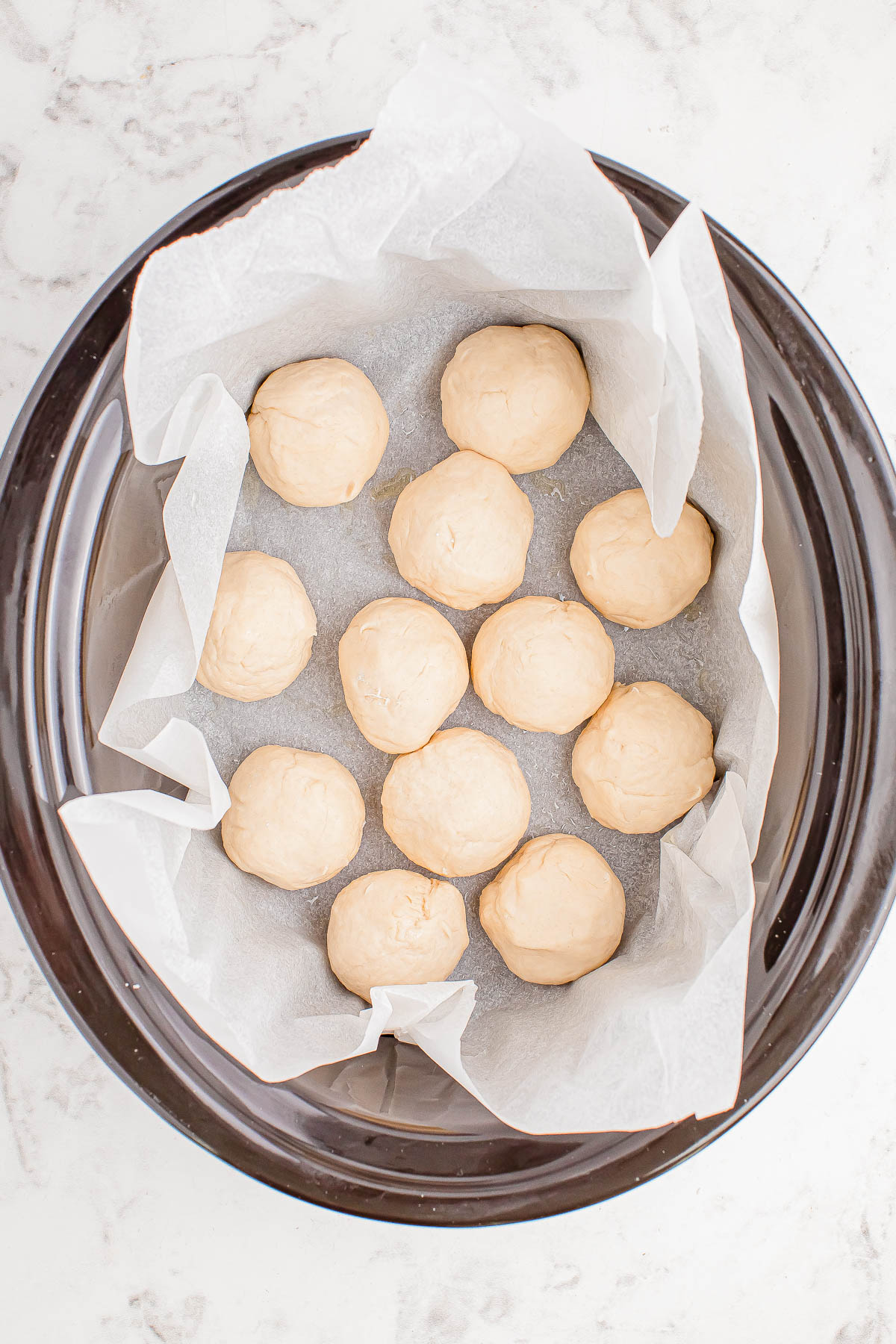 Twelve raw dough balls in a parchment-lined black circular tray on a marble surface.