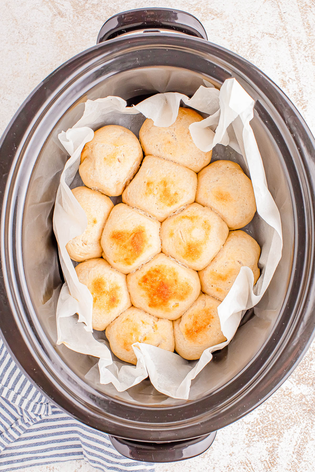 Freshly baked bread rolls arranged on parchment paper inside a slow cooker.