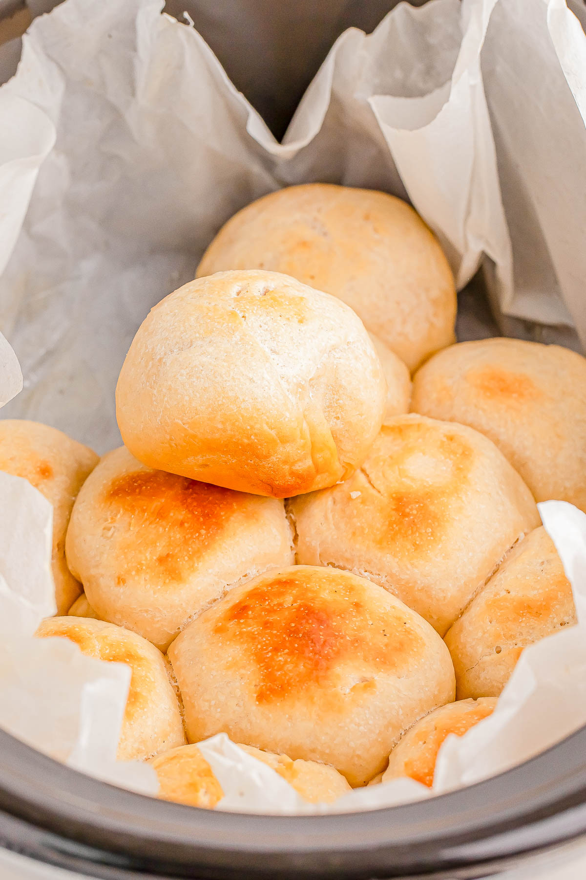 A batch of golden brown dinner rolls on parchment paper in a slow cooker.