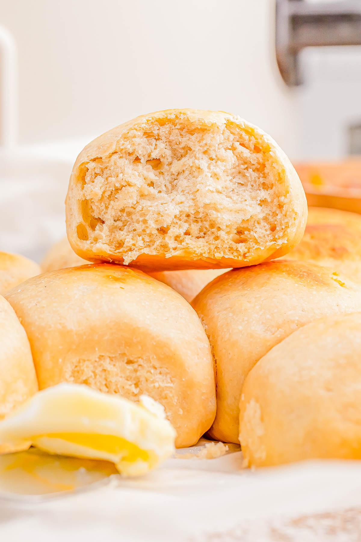 A stack of homemade dinner rolls with a bite taken out of the top one, next to a pat of butter.