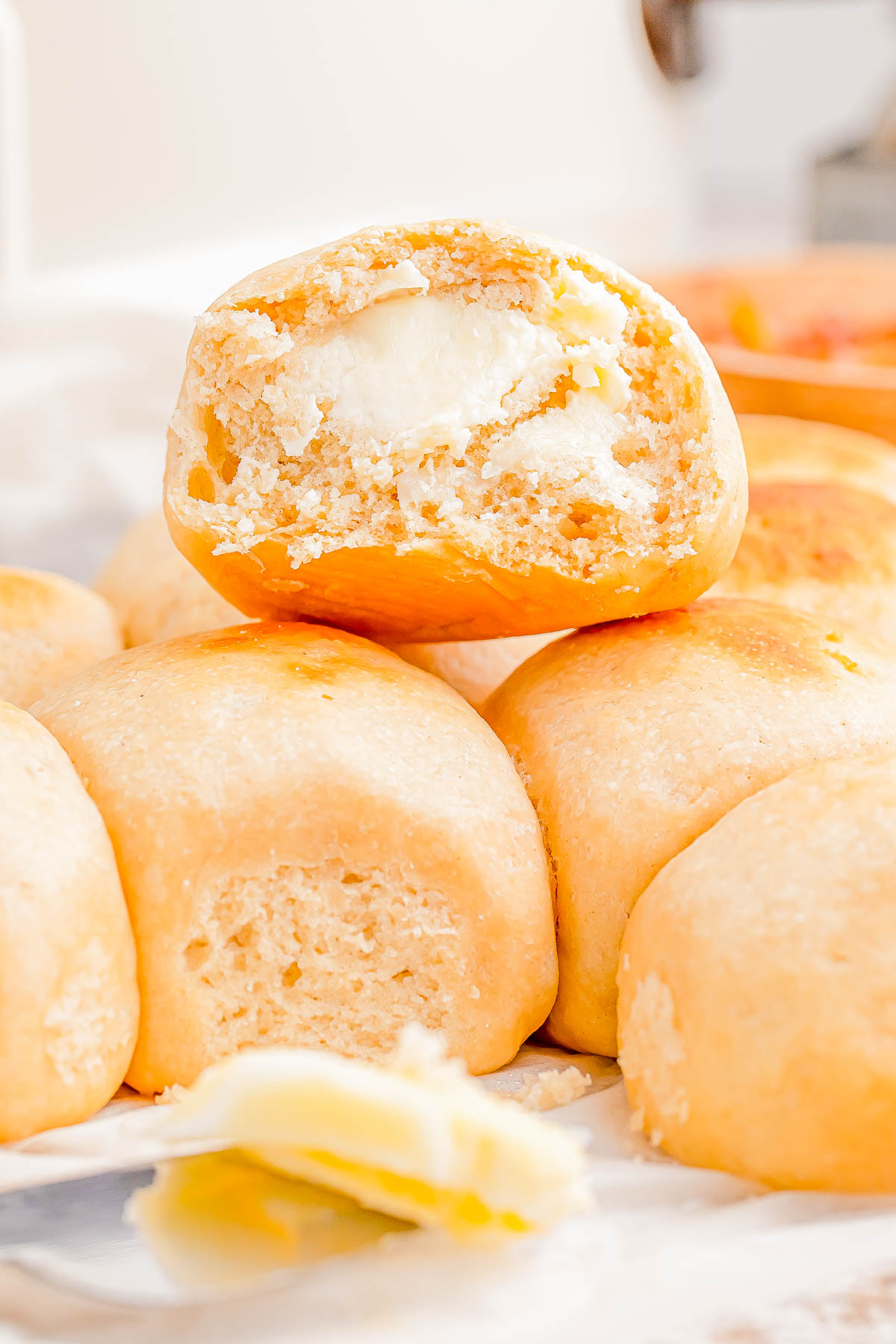 A stack of soft bread rolls, with one roll on top showing a bite revealing a butter-filled center.