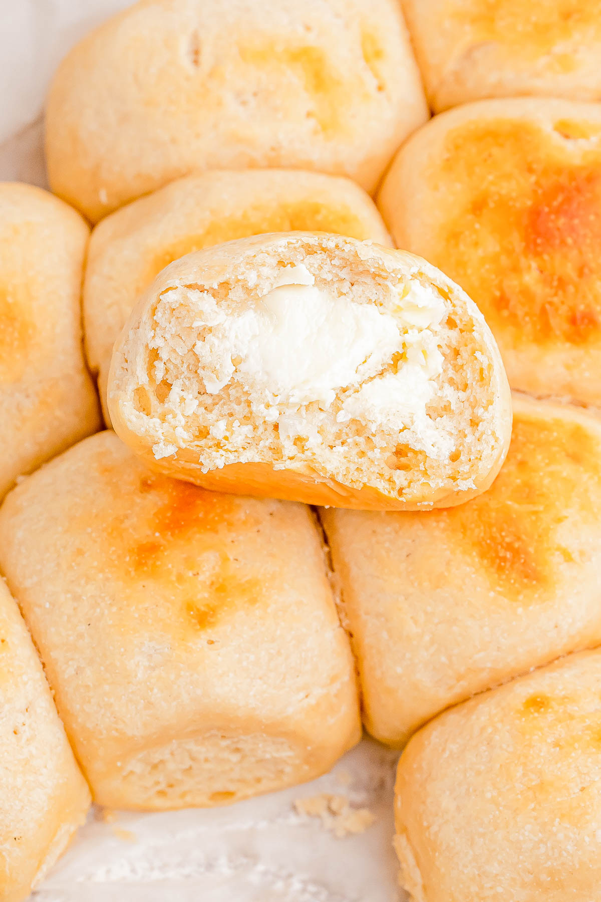 Close-up of freshly baked rolls with one roll bitten to reveal a creamy filling.