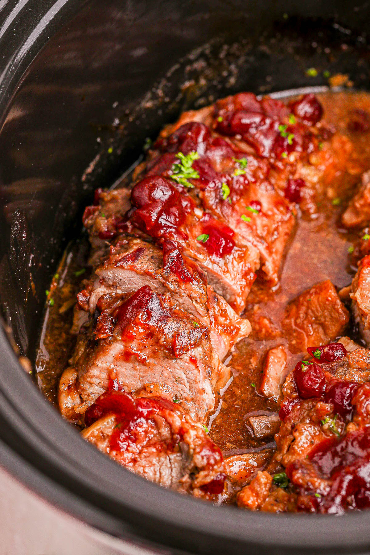 Sliced roast beef topped with a tomato-based sauce and garnished with parsley in a slow cooker.