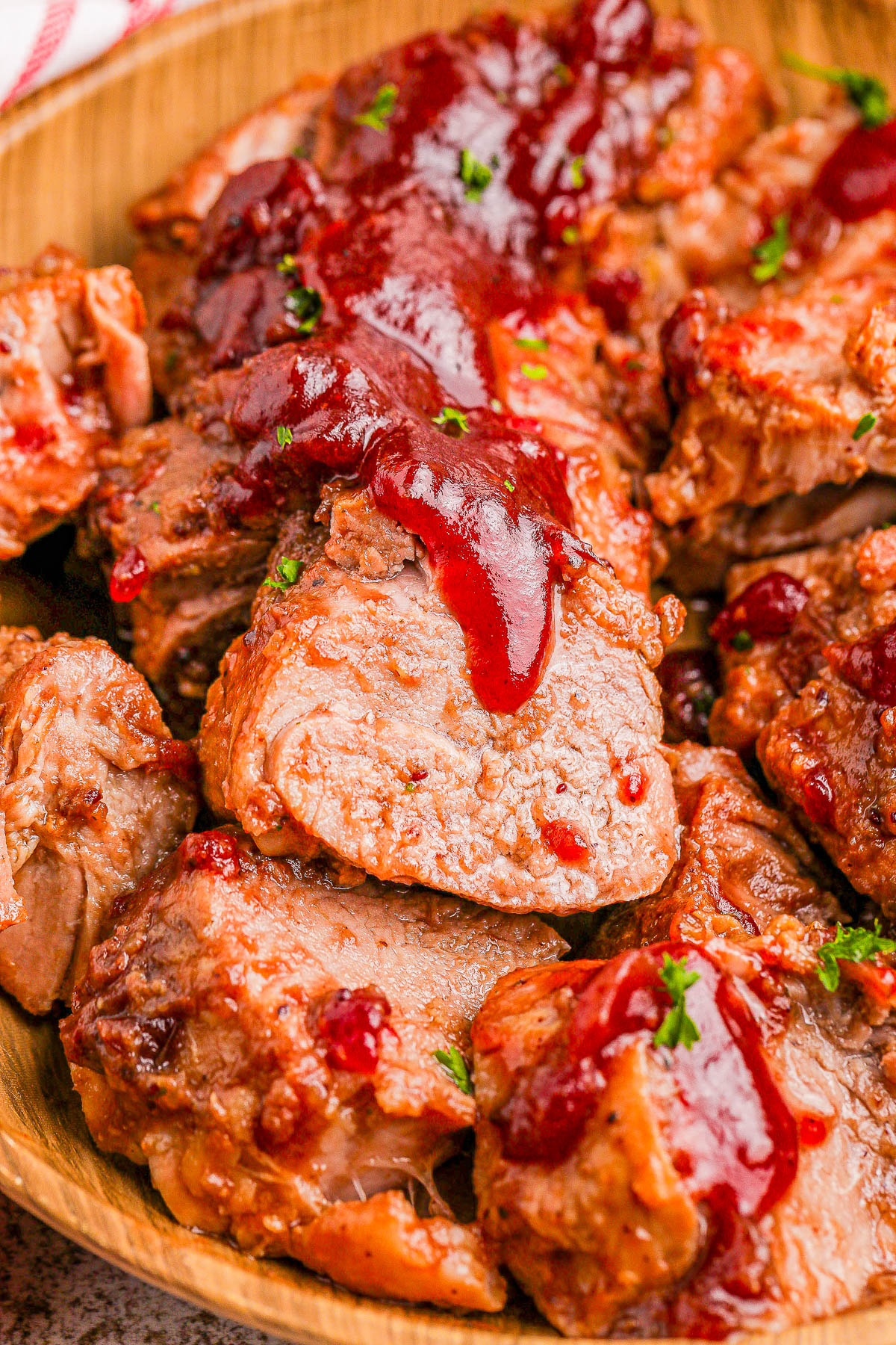 Slices of cooked meat topped with red sauce, garnished with herbs, arranged on a wooden platter.