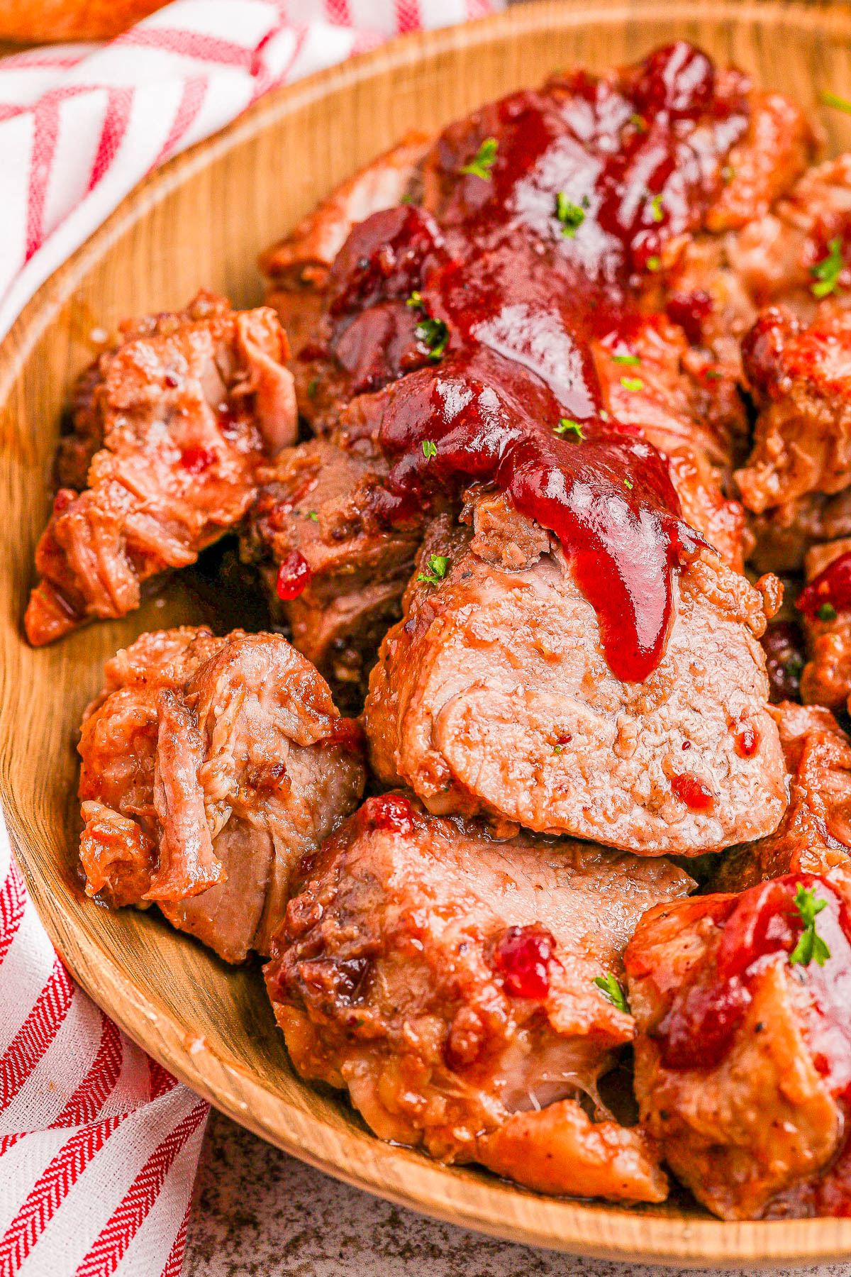 Slices of meat topped with a red sauce on a wooden plate, placed on a striped cloth.