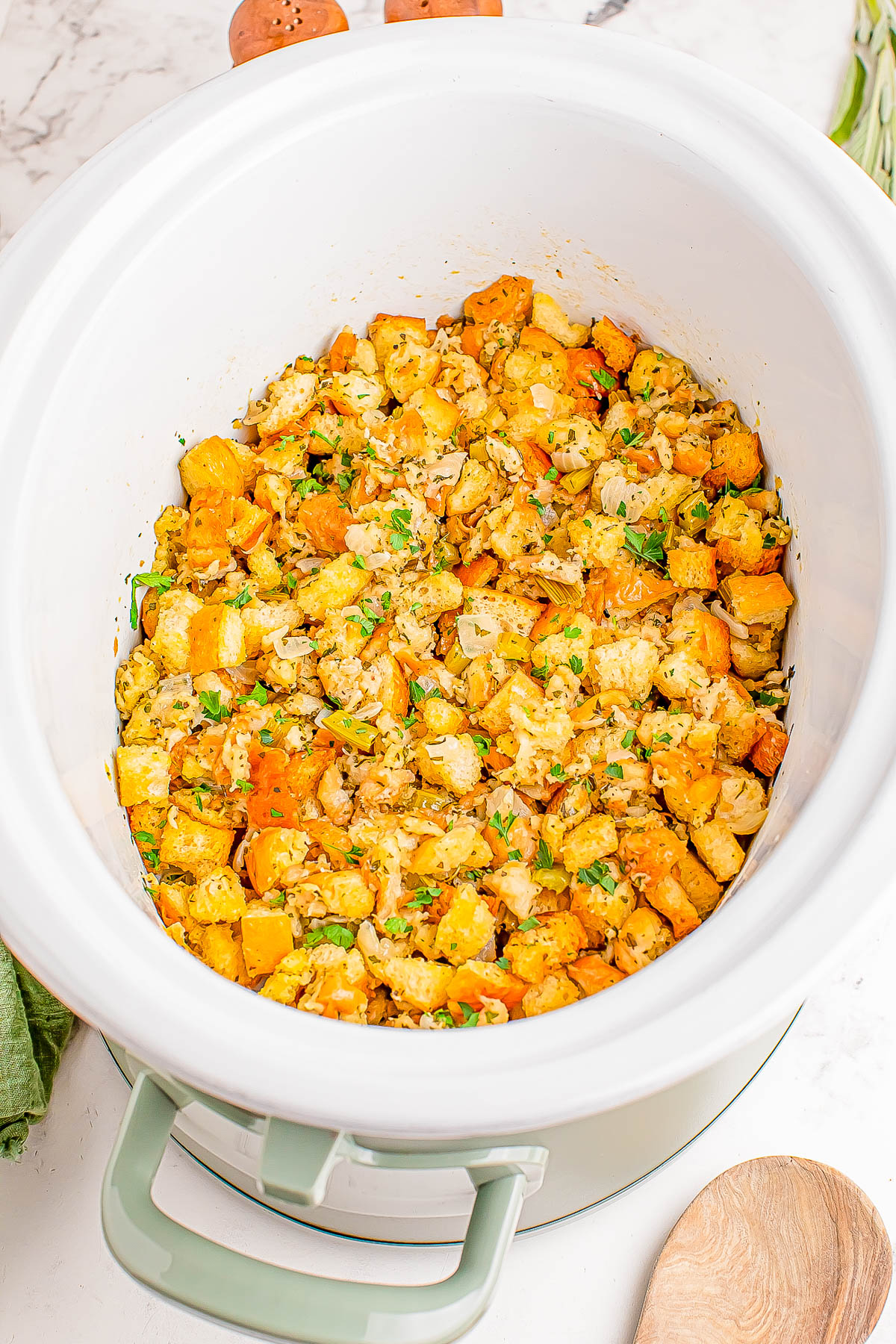 A crockpot filled with seasoned stuffing mix, including diced bread pieces and garnish.