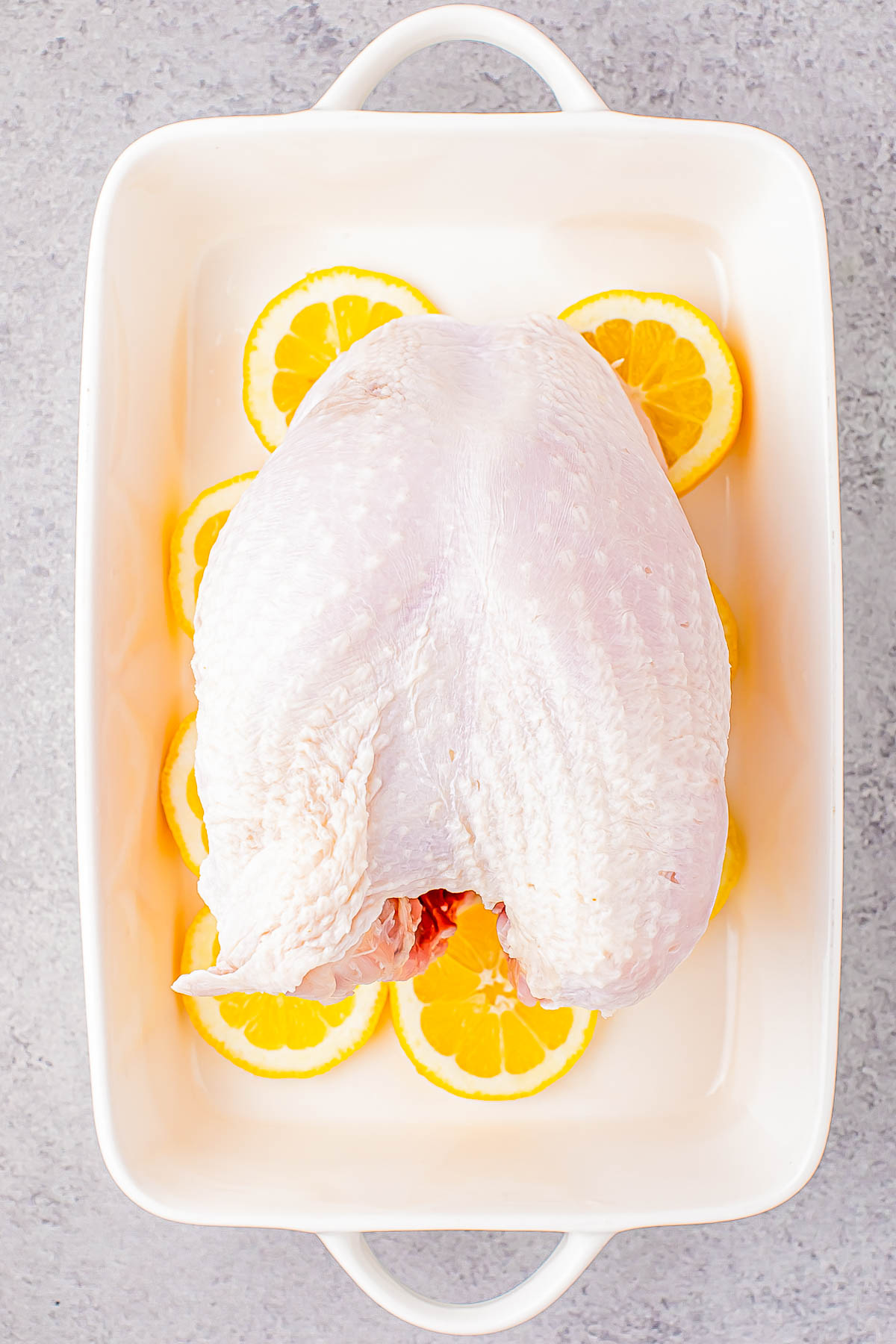 Uncooked turkey breast placed on a bed of lemon slices in a white baking dish.