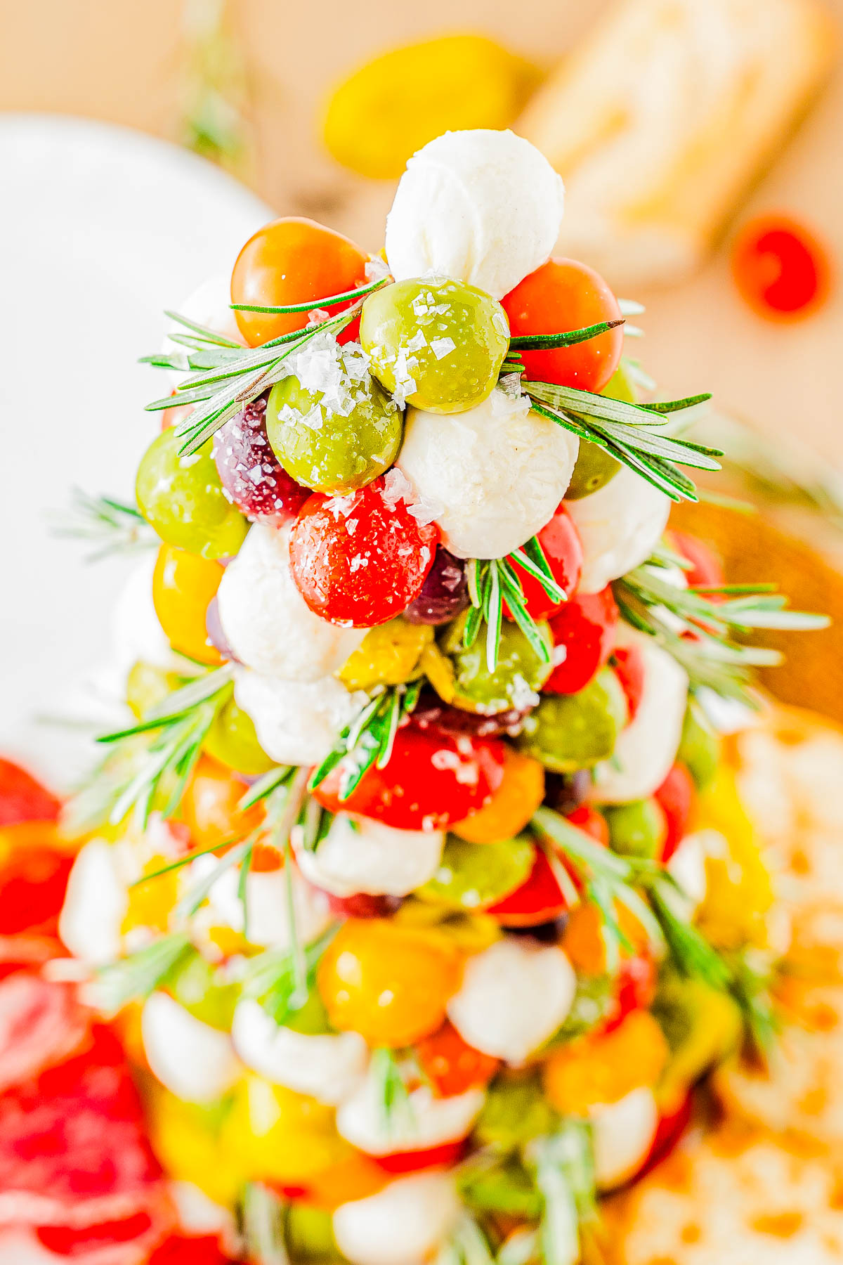 A festive arrangement of cherry tomatoes, mozzarella balls, and olives skewered with rosemary sprigs, forming a tree shape.