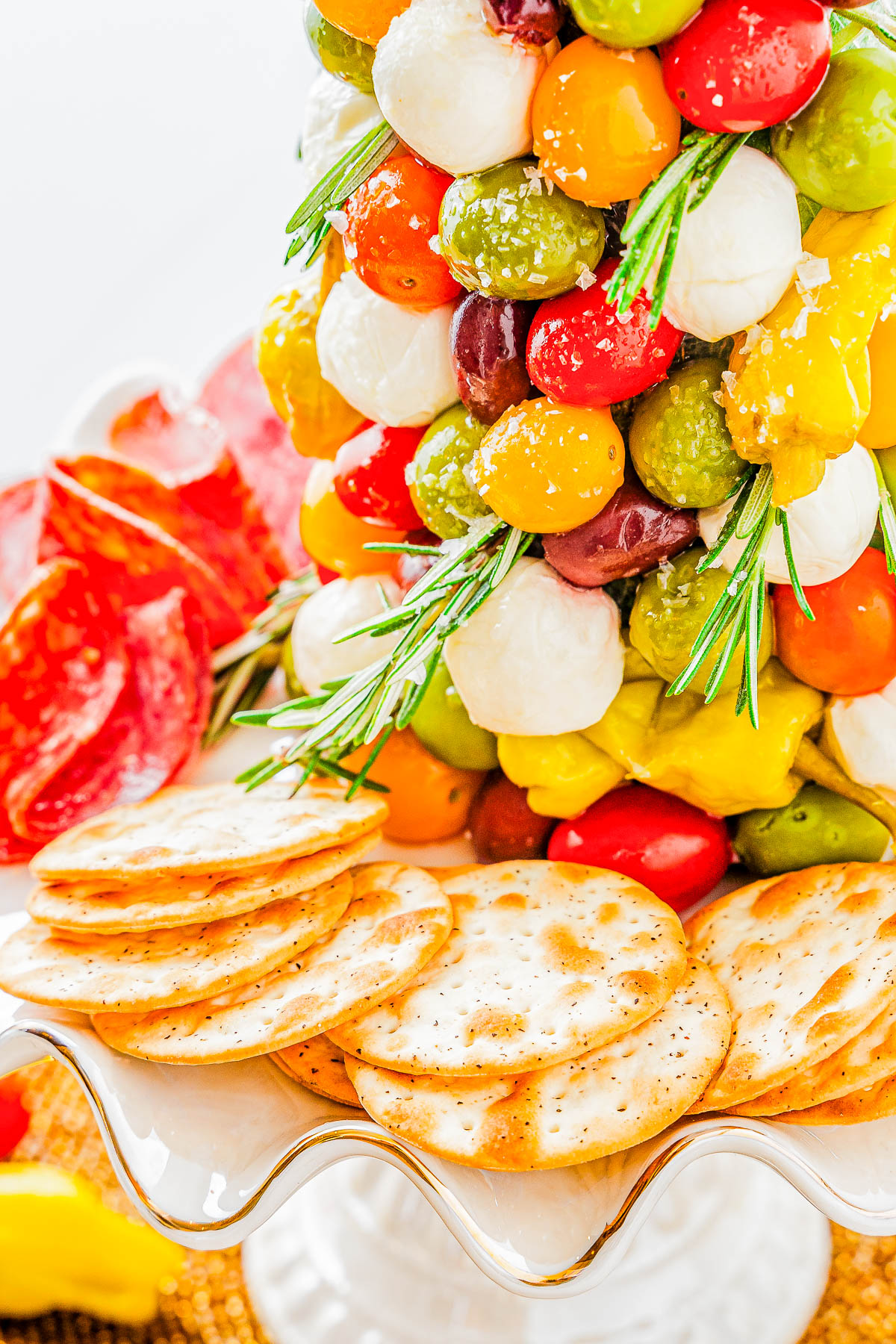 A plate with crackers, salami, and colorful skewered cheeses and olives garnished with rosemary.