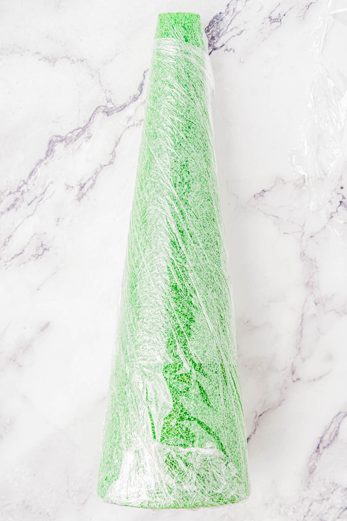 A green glittery cone wrapped in clear plastic sits on a marbled surface.