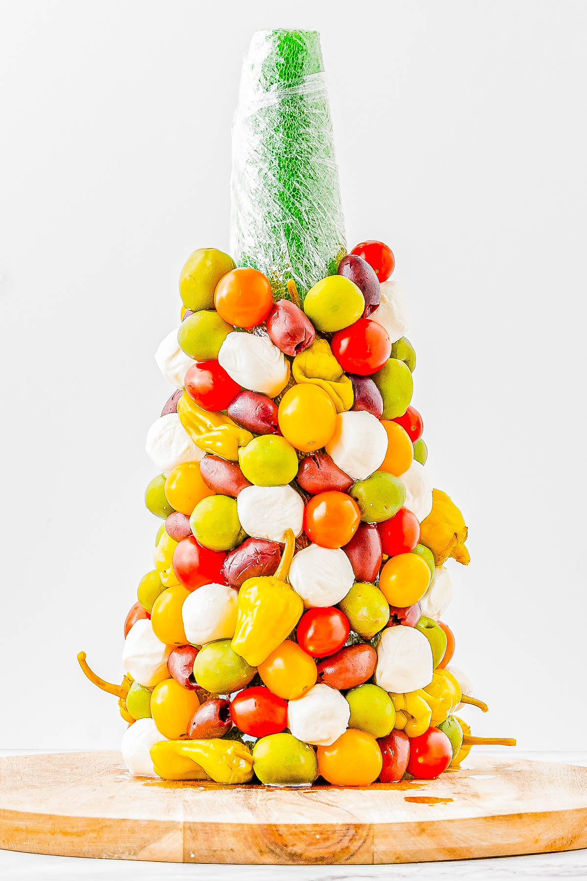 Colorful vegetable and mozzarella cone, featuring cherry tomatoes, round mozzarella, and peppers, arranged on a cone-shaped structure on a wooden base.