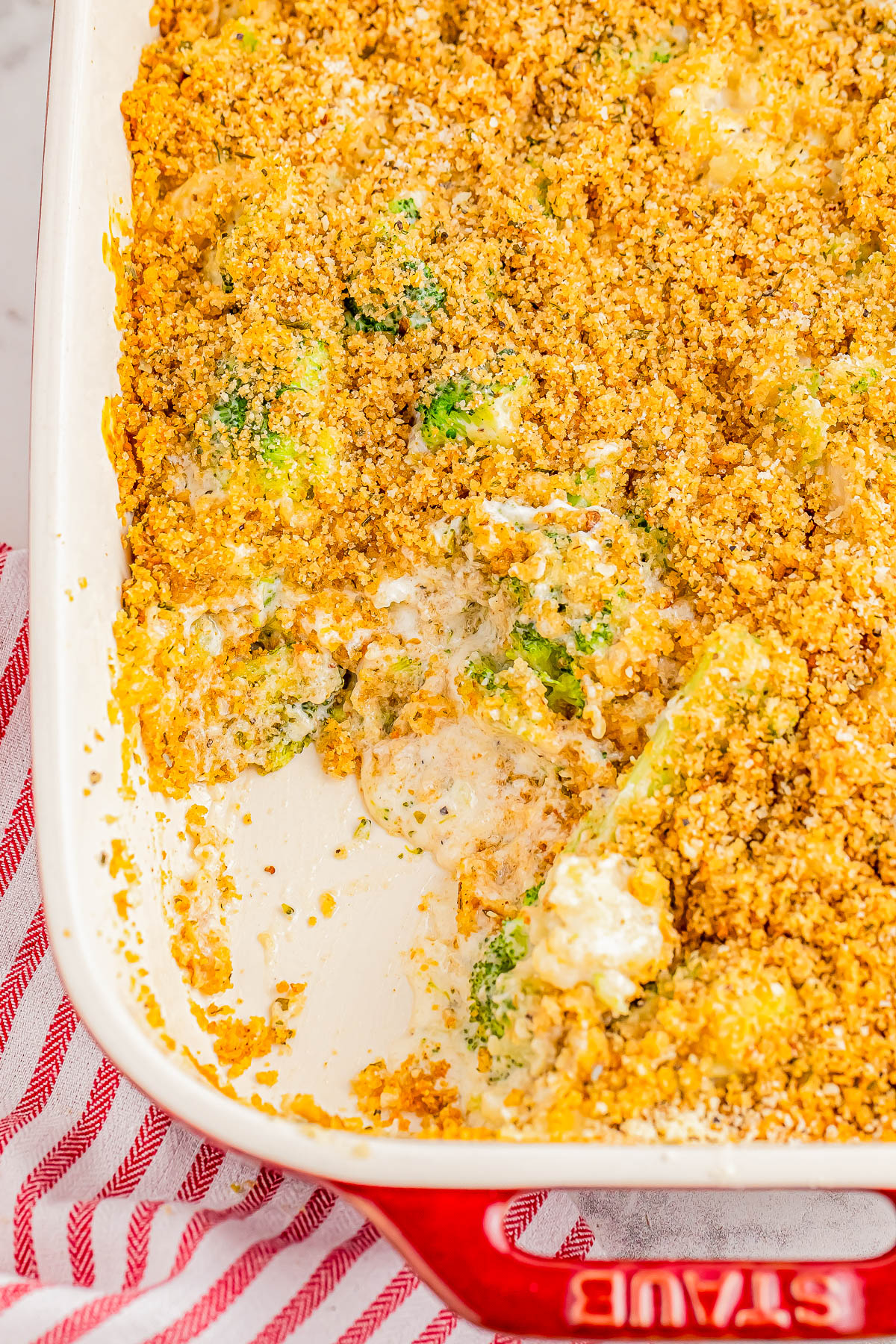 Baked casserole in a red dish, partially eaten, showing a topping of breadcrumbs and visible pieces of vegetables.