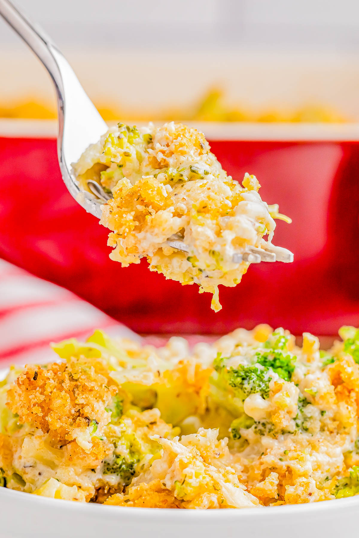 A fork holds a bite of cheesy broccoli casserole with a breadcrumb topping above a dish with more casserole.