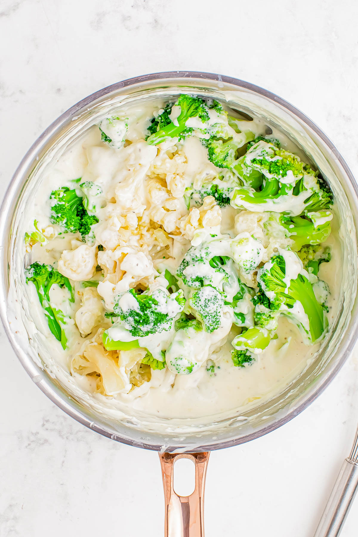 A pan filled with broccoli and cauliflower florets mixed in a creamy white sauce.