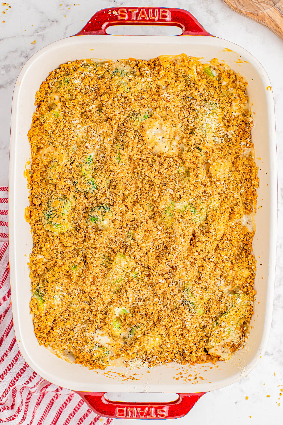 Baked casserole in a rectangular dish with a breadcrumb topping, placed on a marble countertop next to a red-striped cloth.