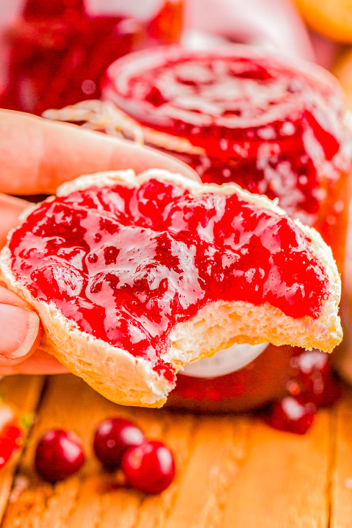 A bitten piece of bread with vibrant red cranberry jam, held by a hand.