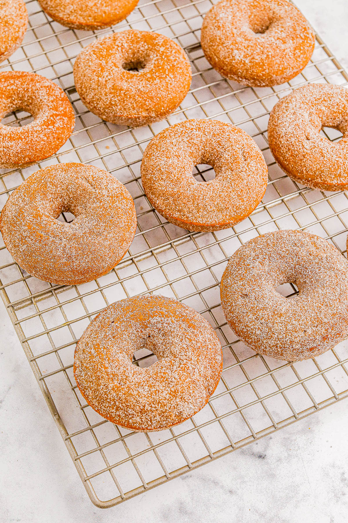 A cooling rack with nine sugar-coated donuts arranged in rows.