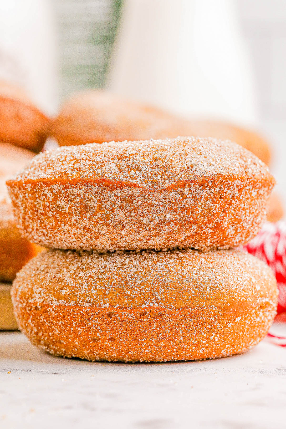 Two sugar-coated donuts are stacked on top of each other on a white surface.