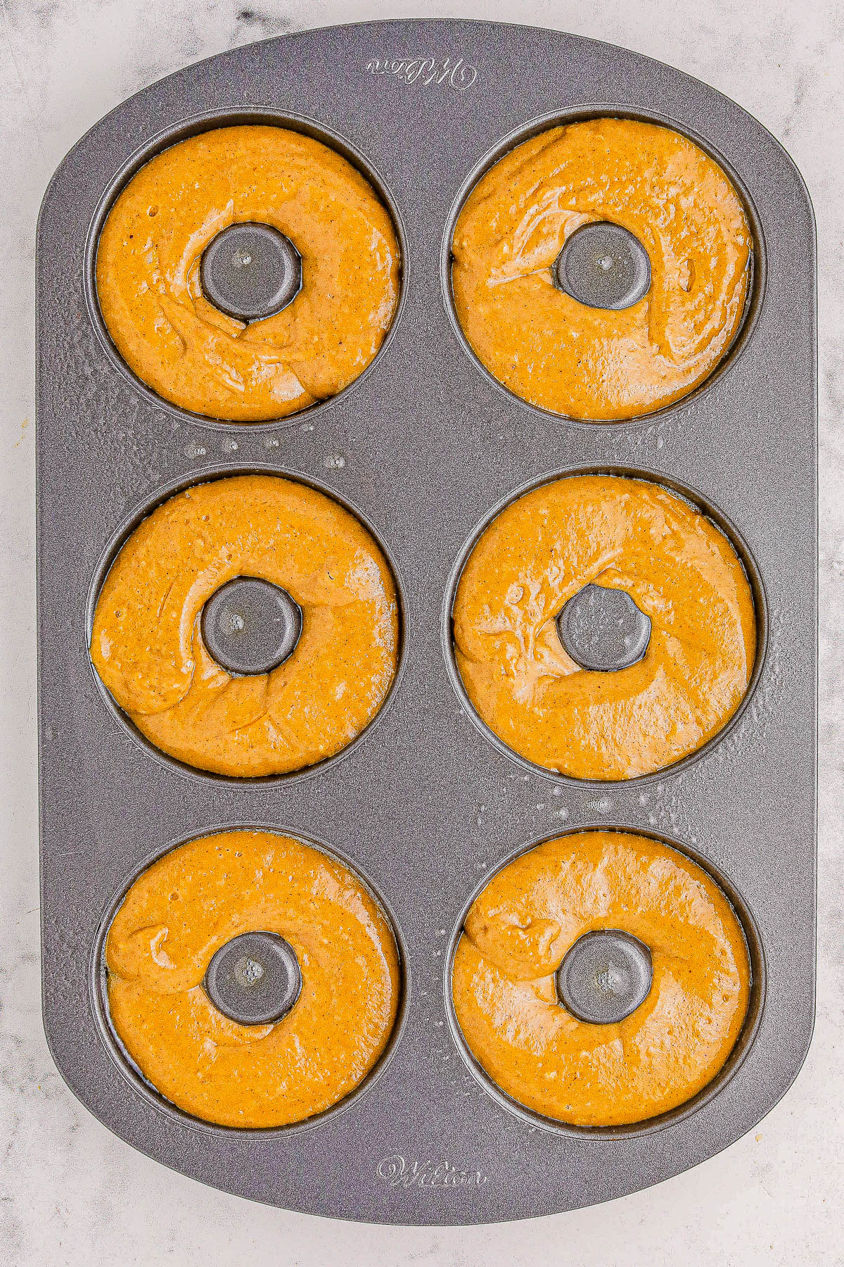 A six-cavity donut pan filled with unbaked batter, ready for the oven.