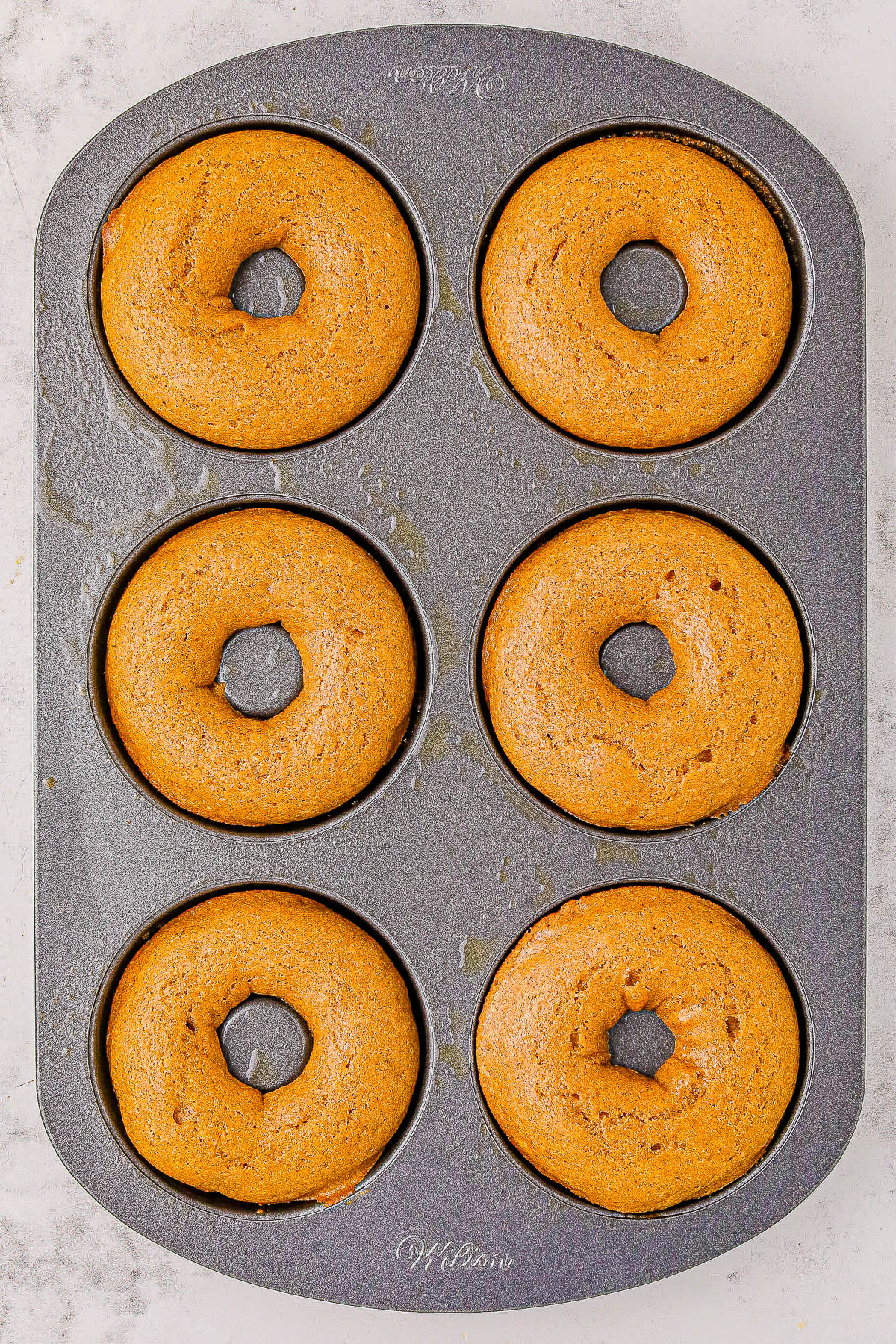 Six freshly baked donuts in a metal donut pan.