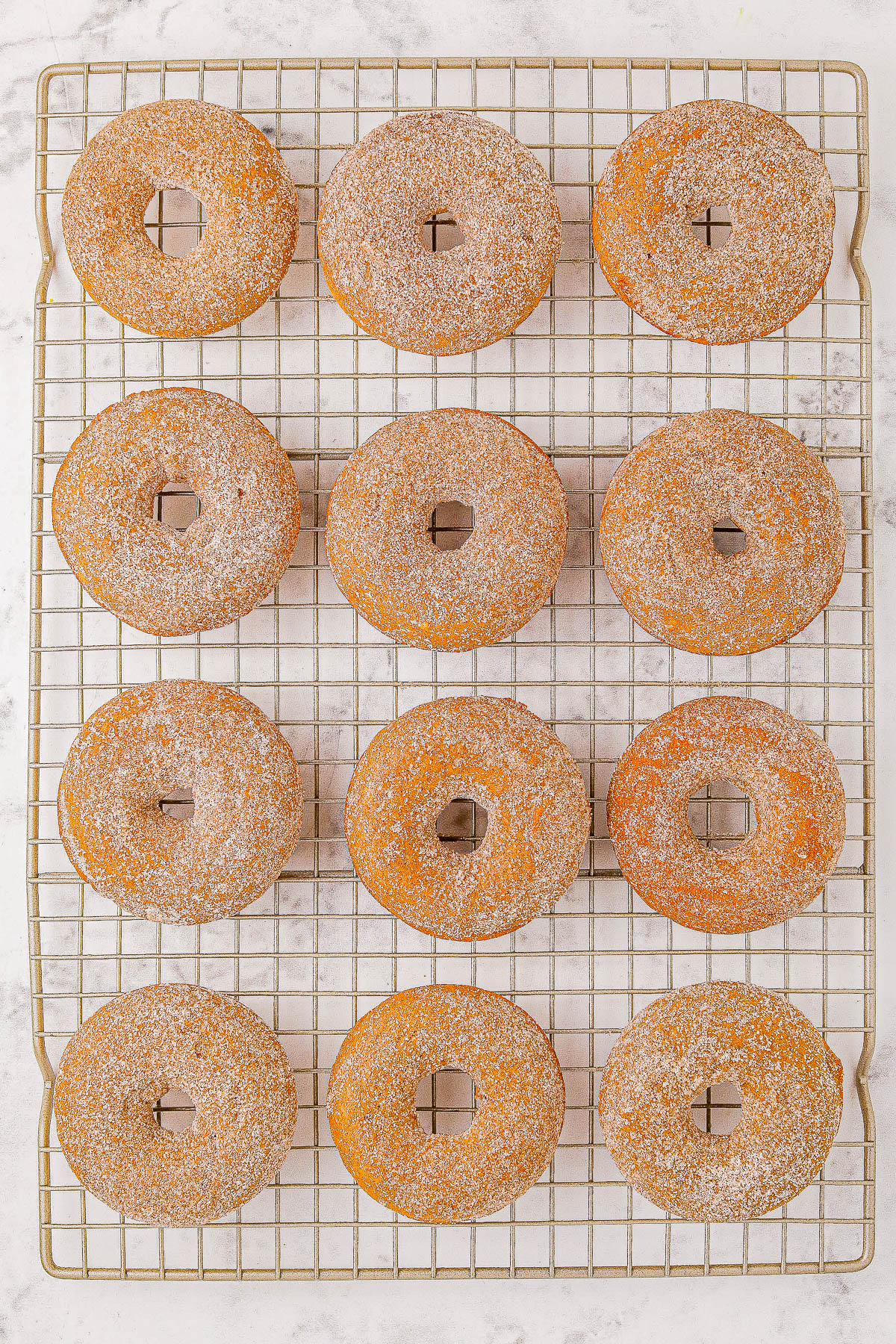 Twelve sugar-coated doughnuts on a wire cooling rack.