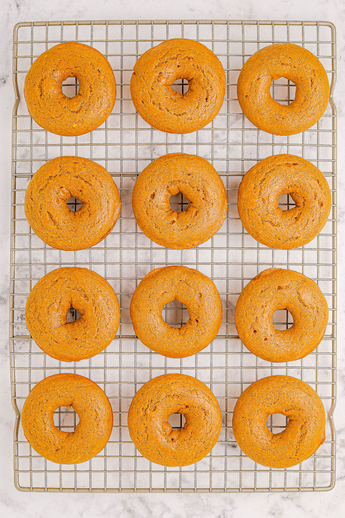 Twelve baked donuts arranged in rows on a cooling rack.