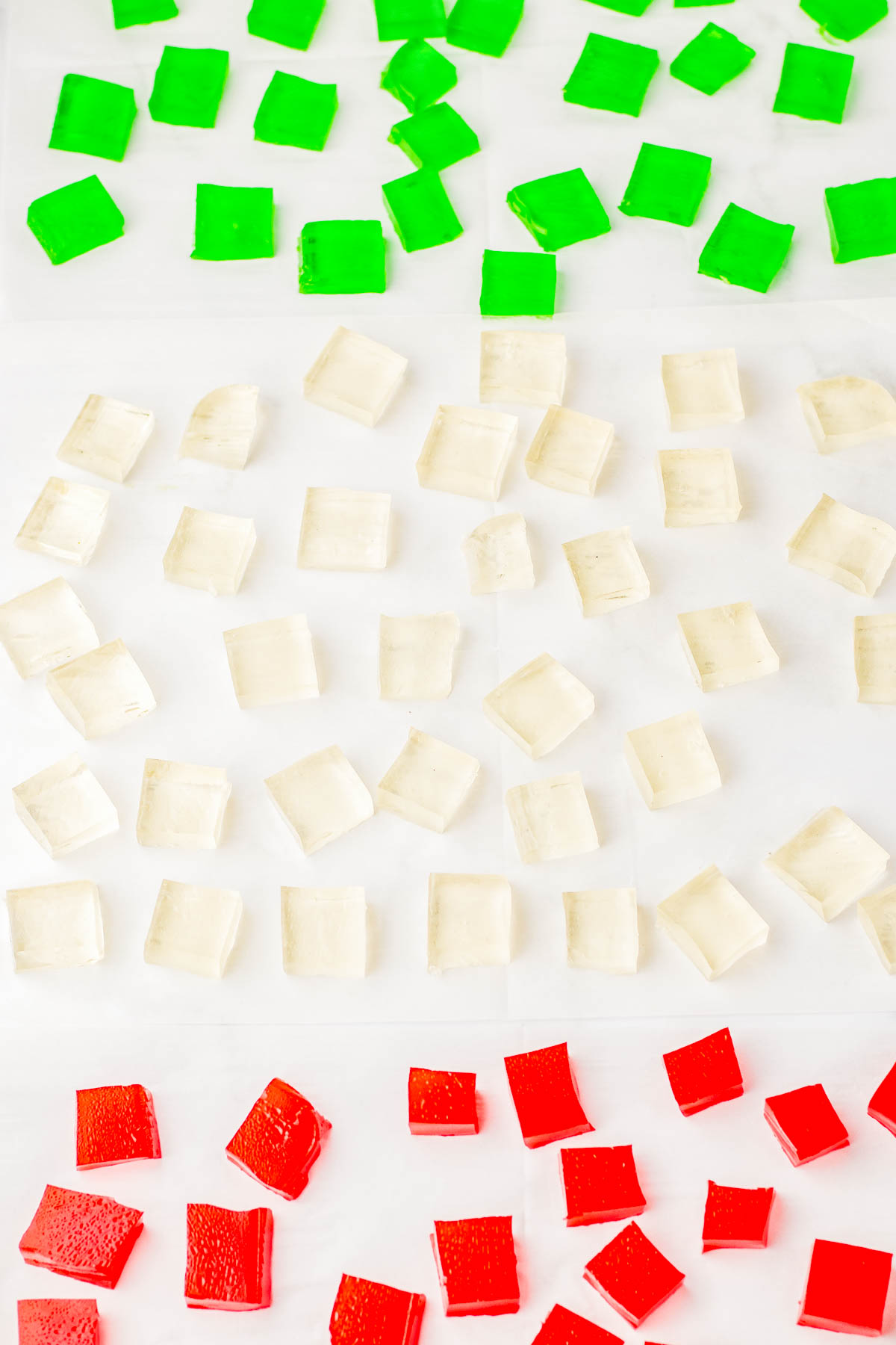 Green, clear, and red square jelly pieces arranged in neat rows on a light surface.