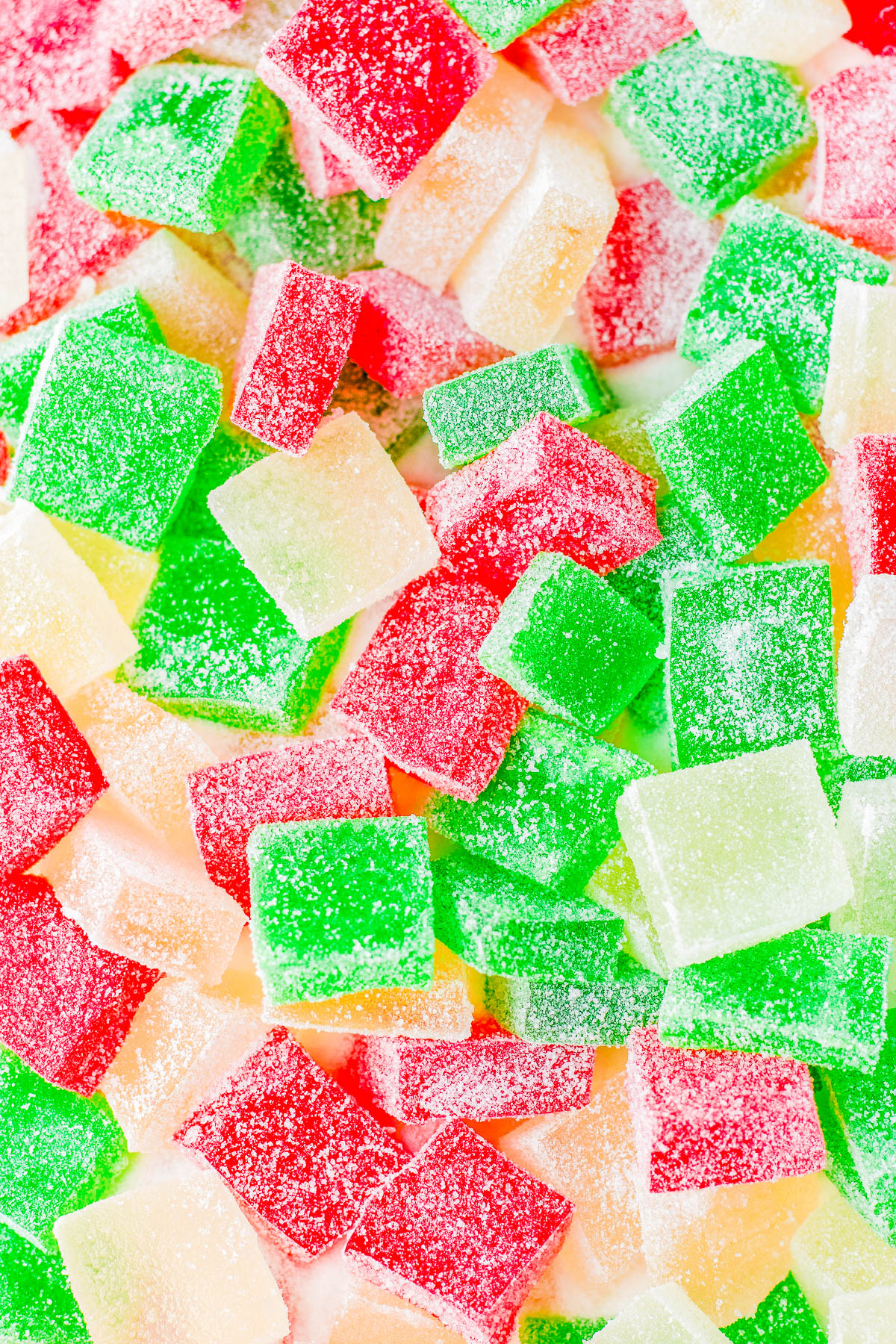 Colorful sugar-coated gummy squares in red, green, and yellow are piled together.