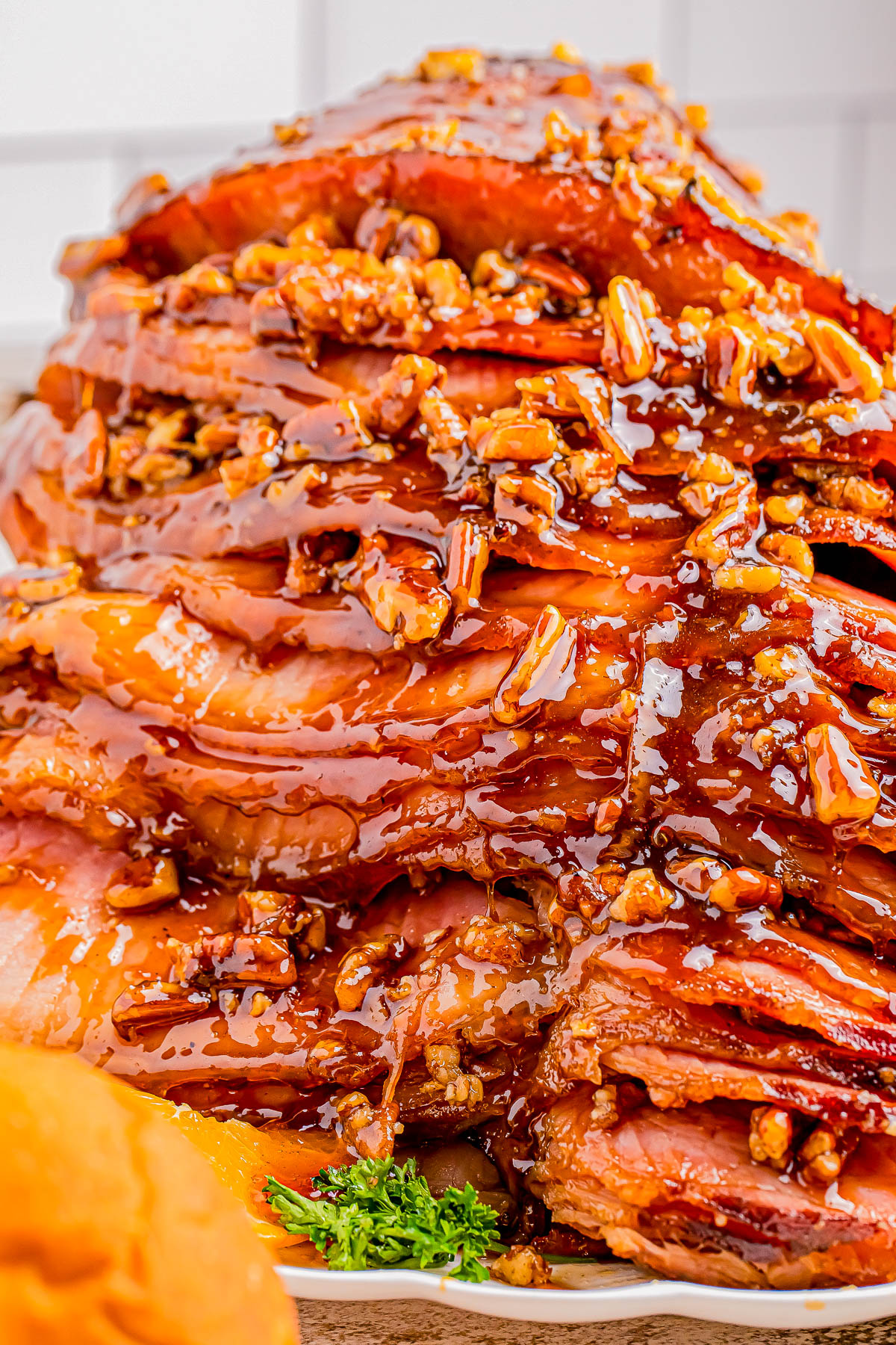 Sliced ham glazed with a glossy sauce and topped with chopped pecans, served on a white plate with parsley garnish.