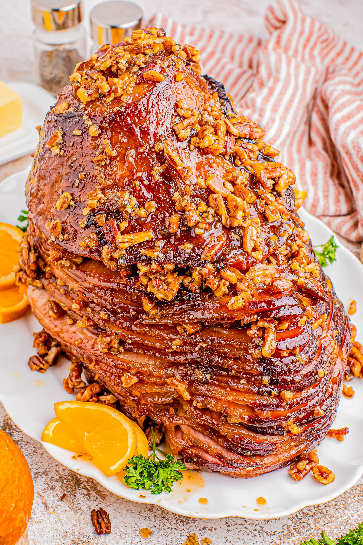 Glazed ham topped with chopped pecans, garnished with orange slices and parsley on a white platter.