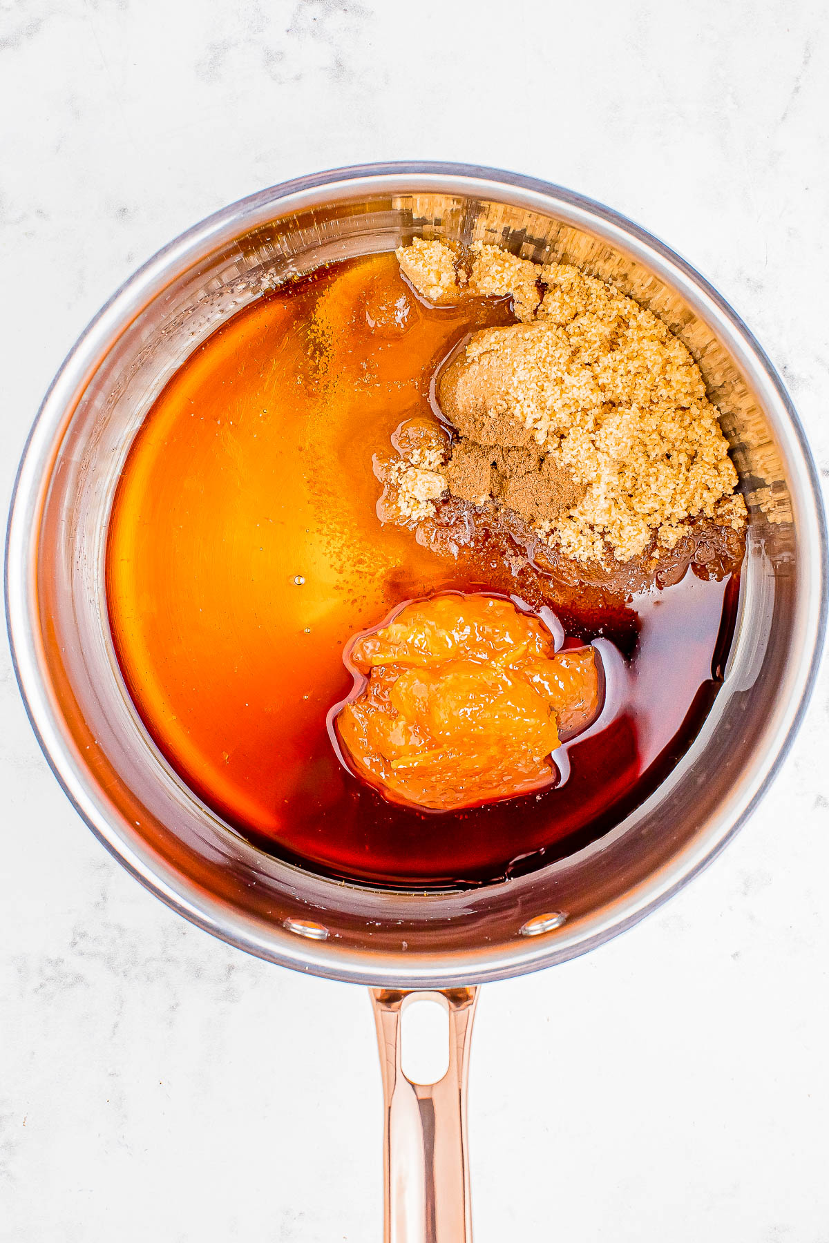 Saucepan with brown sugar, honey, and molasses on a light surface, ready for mixing or cooking.