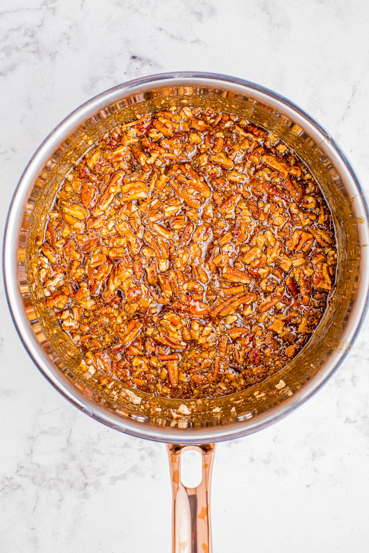 Close-up of a saucepan containing a golden-brown mixture of chopped pecans and syrup.