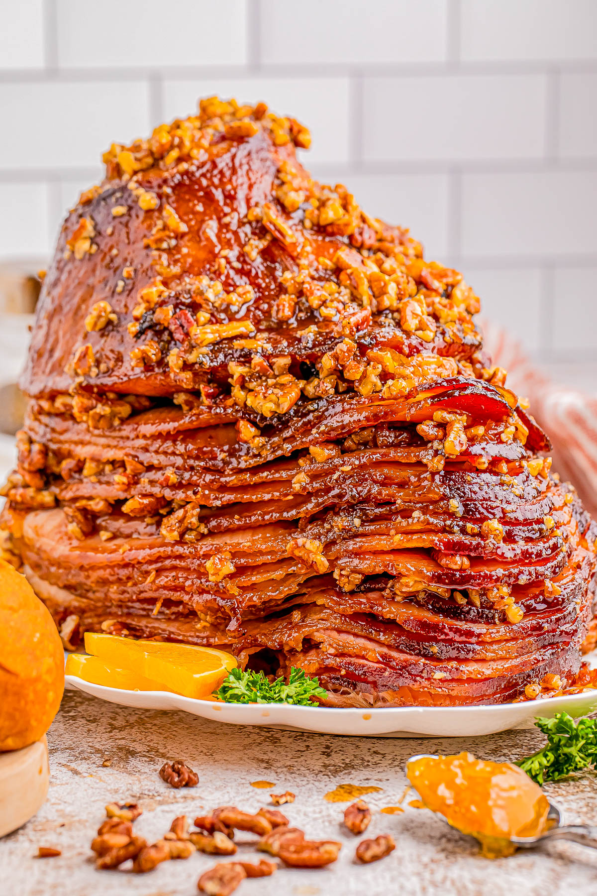 A glazed ham covered with chopped nuts is presented on a plate, garnished with orange slices and parsley.