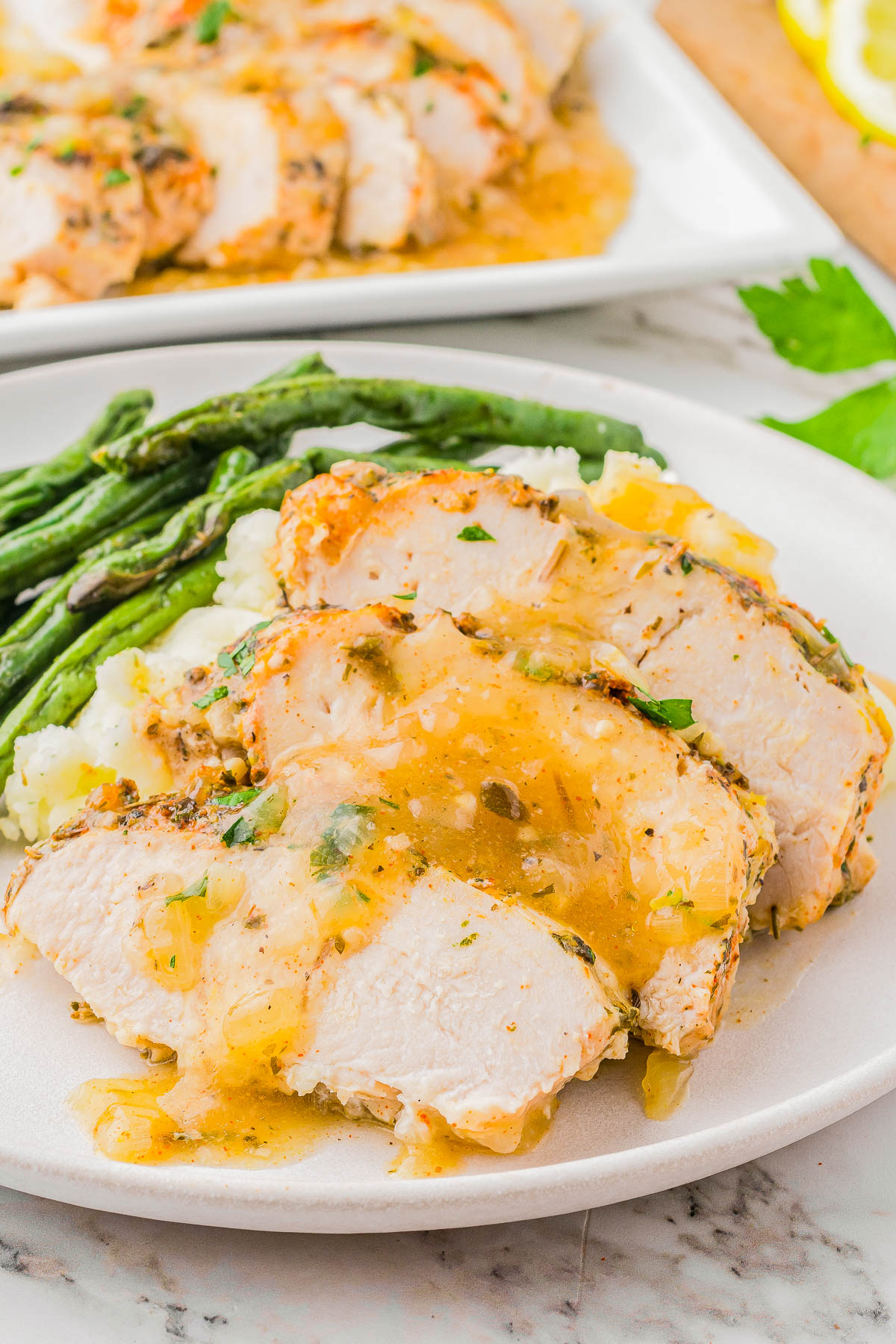 Slices of grilled chicken breast with sauce, served on mashed potatoes and green beans, on a white plate.