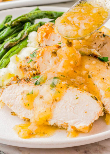 Sliced turkey breast with gravy on a white plate, served with mashed potatoes and asparagus.