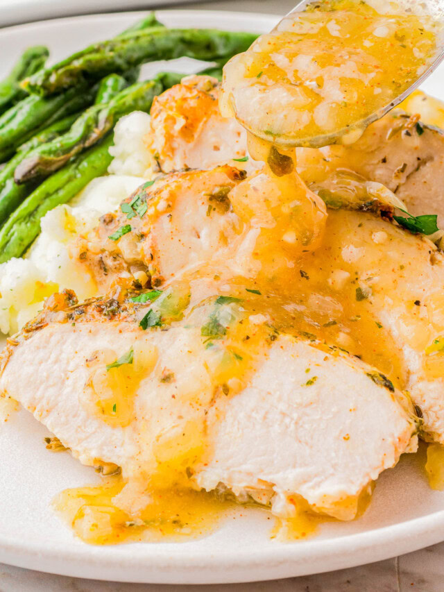 Sliced turkey breast with gravy on a white plate, served with mashed potatoes and asparagus.