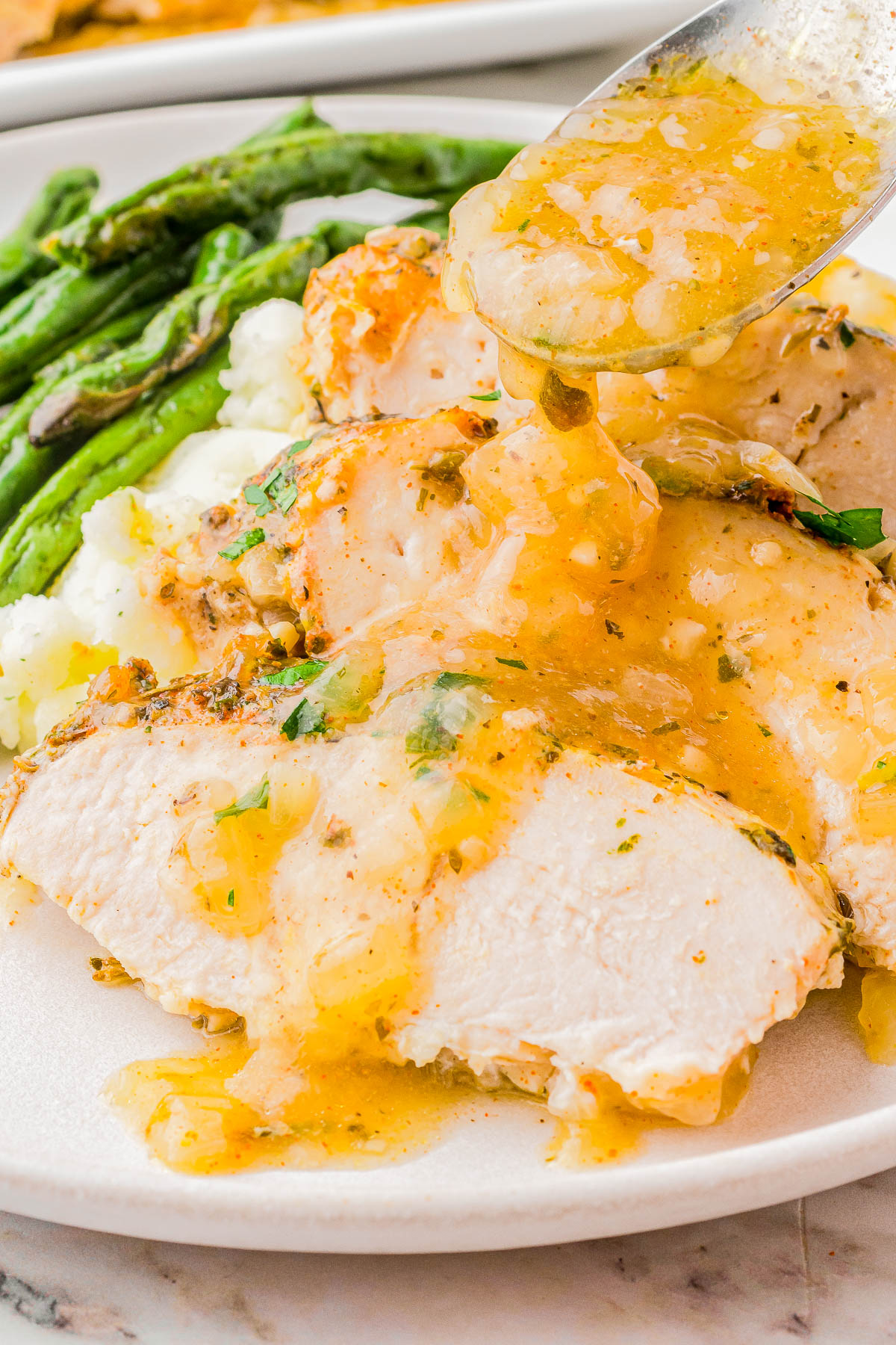 Sliced turkey breast with gravy on a white plate, served with mashed potatoes and asparagus.