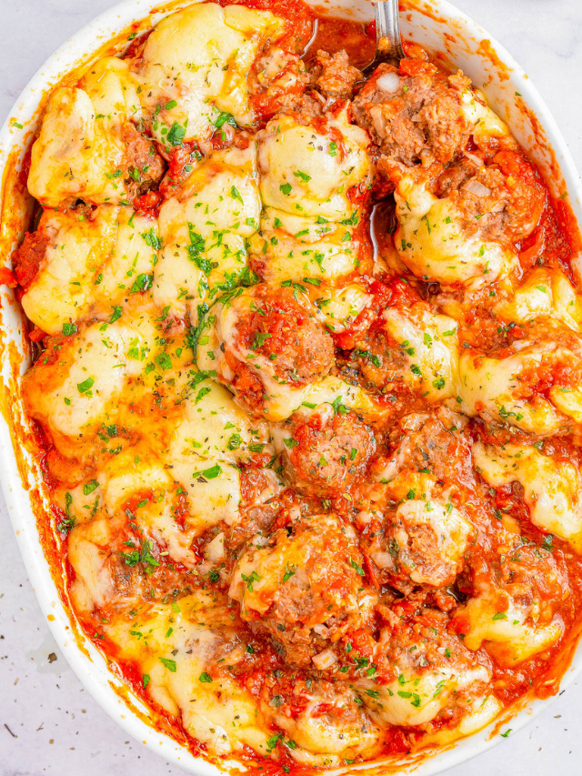 Close-up of a baked dish with meatballs, tomato sauce, melted cheese, and sprinkled herbs in a white oval dish.