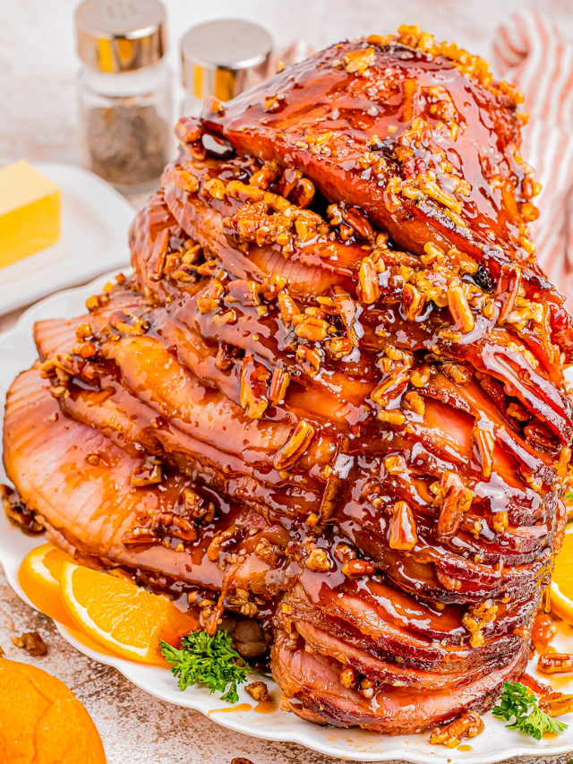 A glazed, sliced ham garnished with orange slices and parsley on a platter. Peppershakers and butter are in the background.