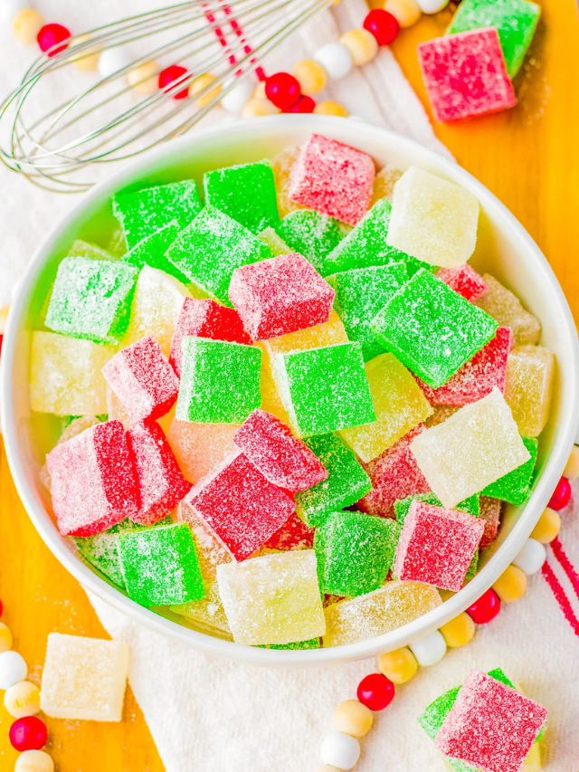 A bowl of colorful sugar-coated gummy cubes in green, red, and yellow. A whisk and beaded decorations are visible in the background.