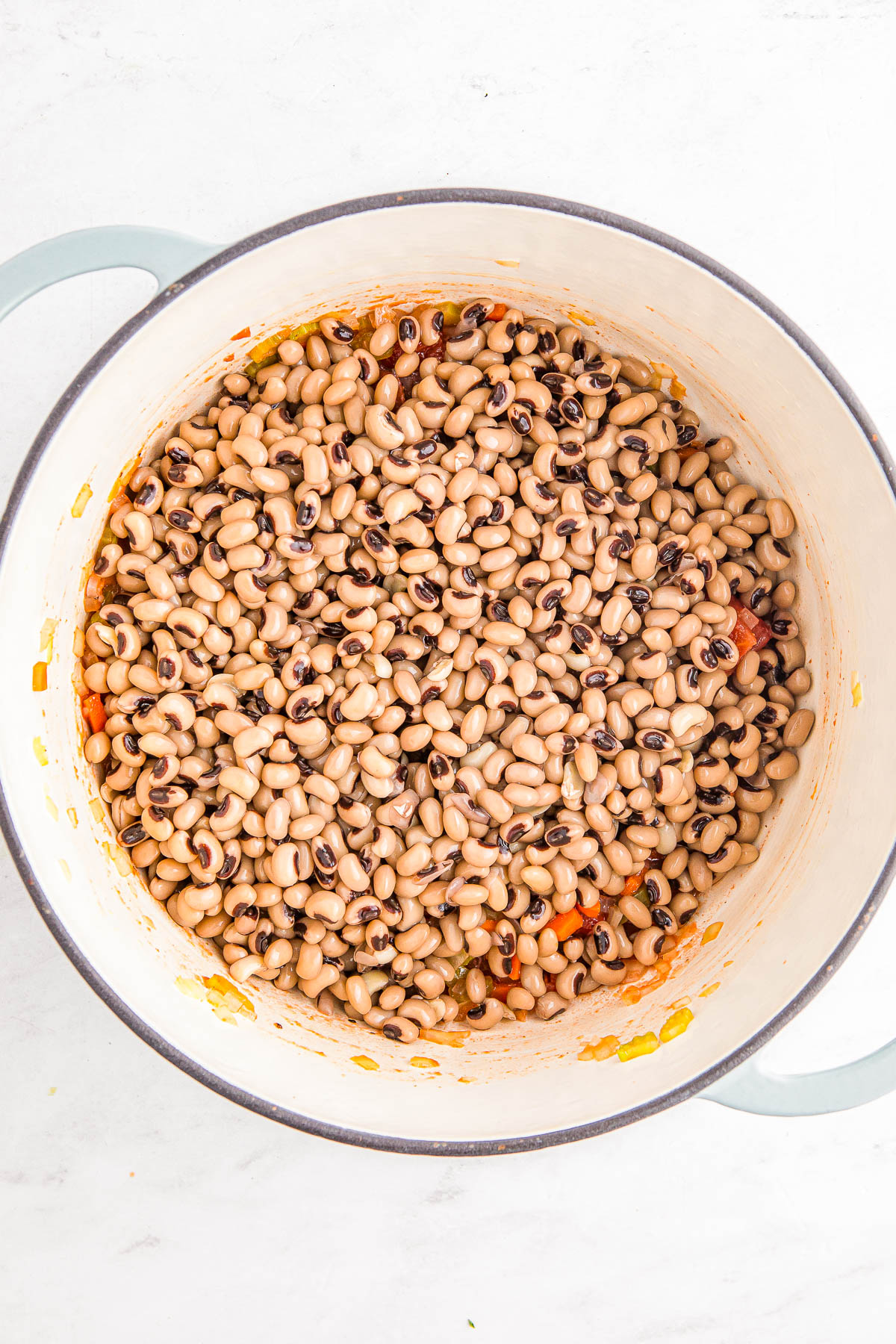 A pot filled with cooked black-eyed peas mixed with small pieces of vegetables on a light surface.