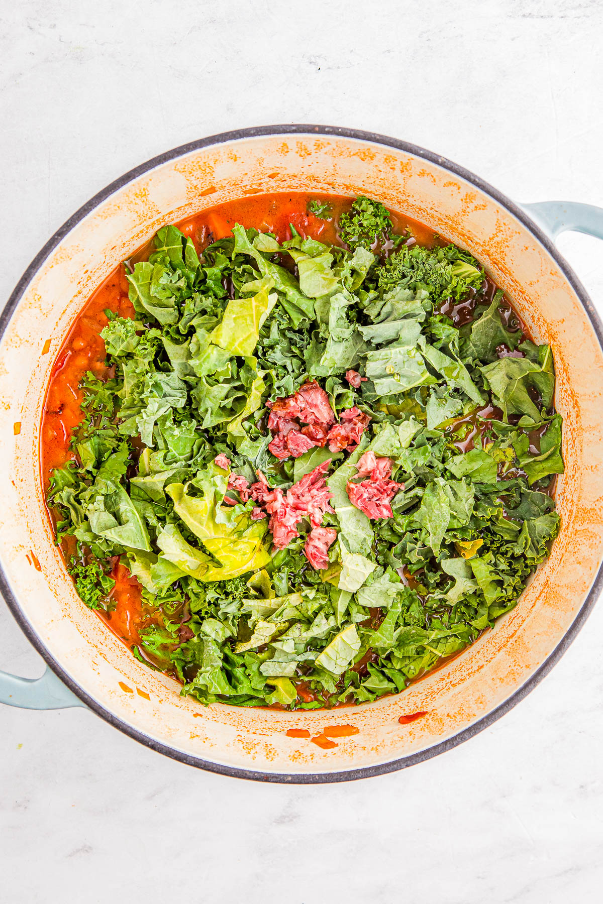 A pot filled with leafy greens and diced ingredients, possibly meat, in a red broth.