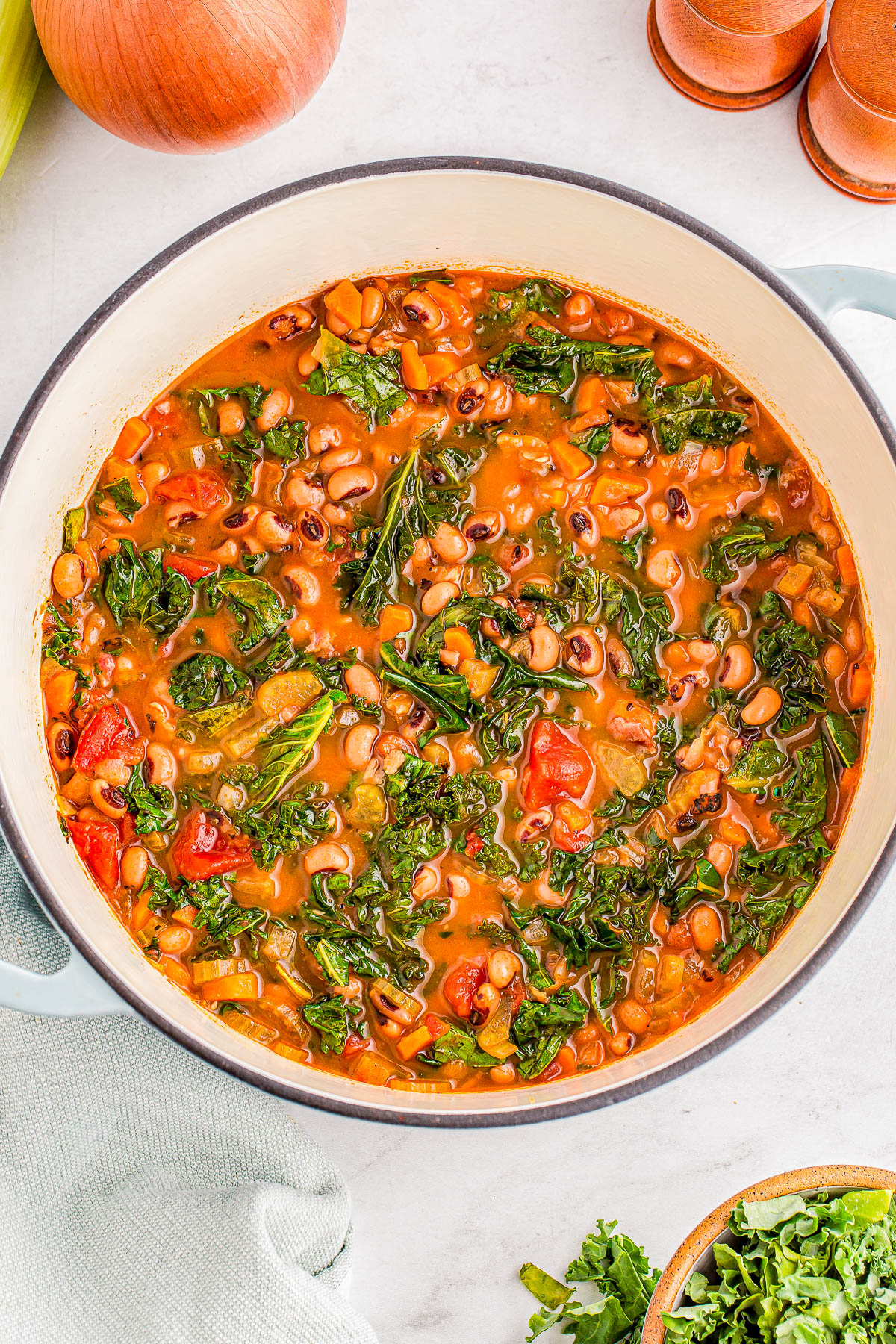 A pot of vegetable stew with black-eyed peas, kale, tomatoes, and carrots on a light countertop.