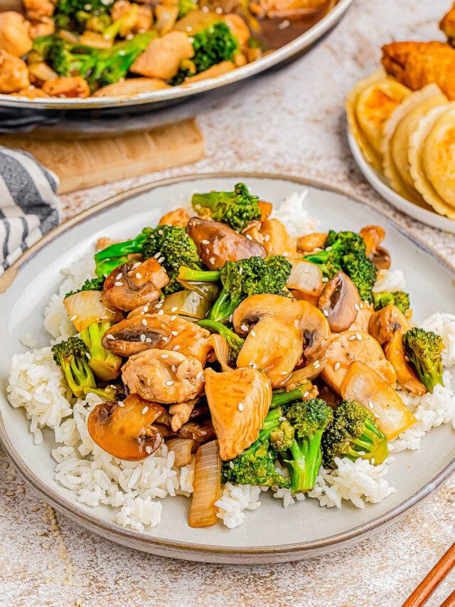 A plate of stir-fried chicken, mushrooms, and broccoli served over white rice. Nearby, there is a plate with dumplings and fried chicken.