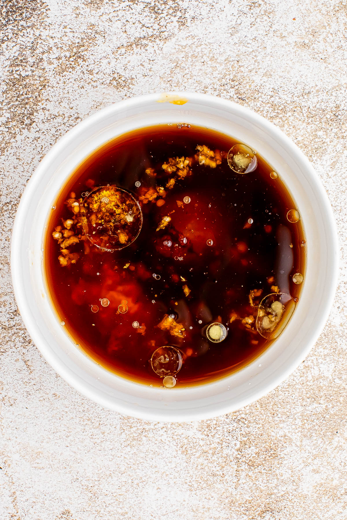 A white bowl filled with a dark liquid sauce containing pieces of chopped garlic and visible oil droplets on the surface.